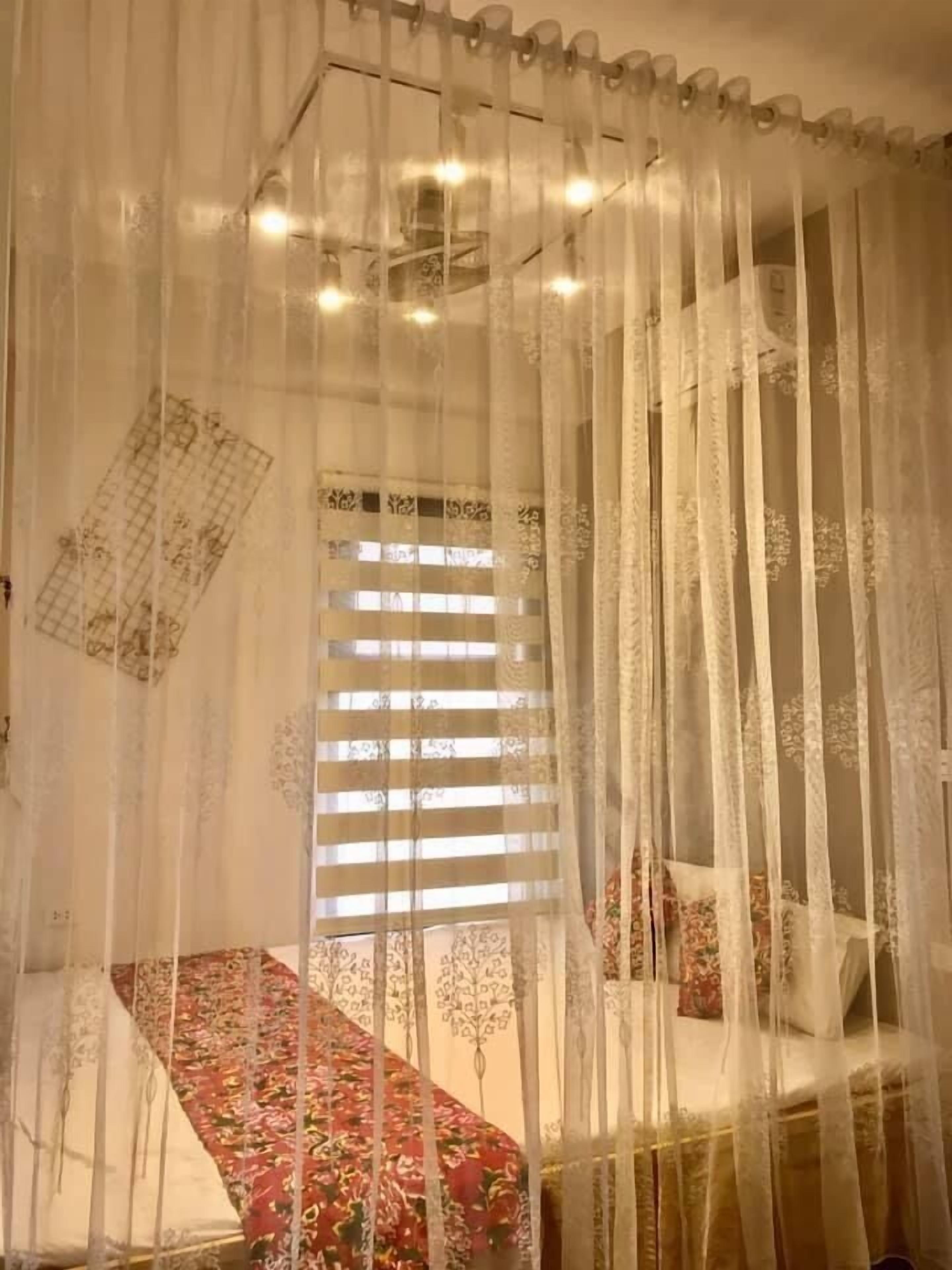 Una habitación con una cama cubierta con ropa de cama estampada, una ventana con persianas y una cortina de diseño calado.
