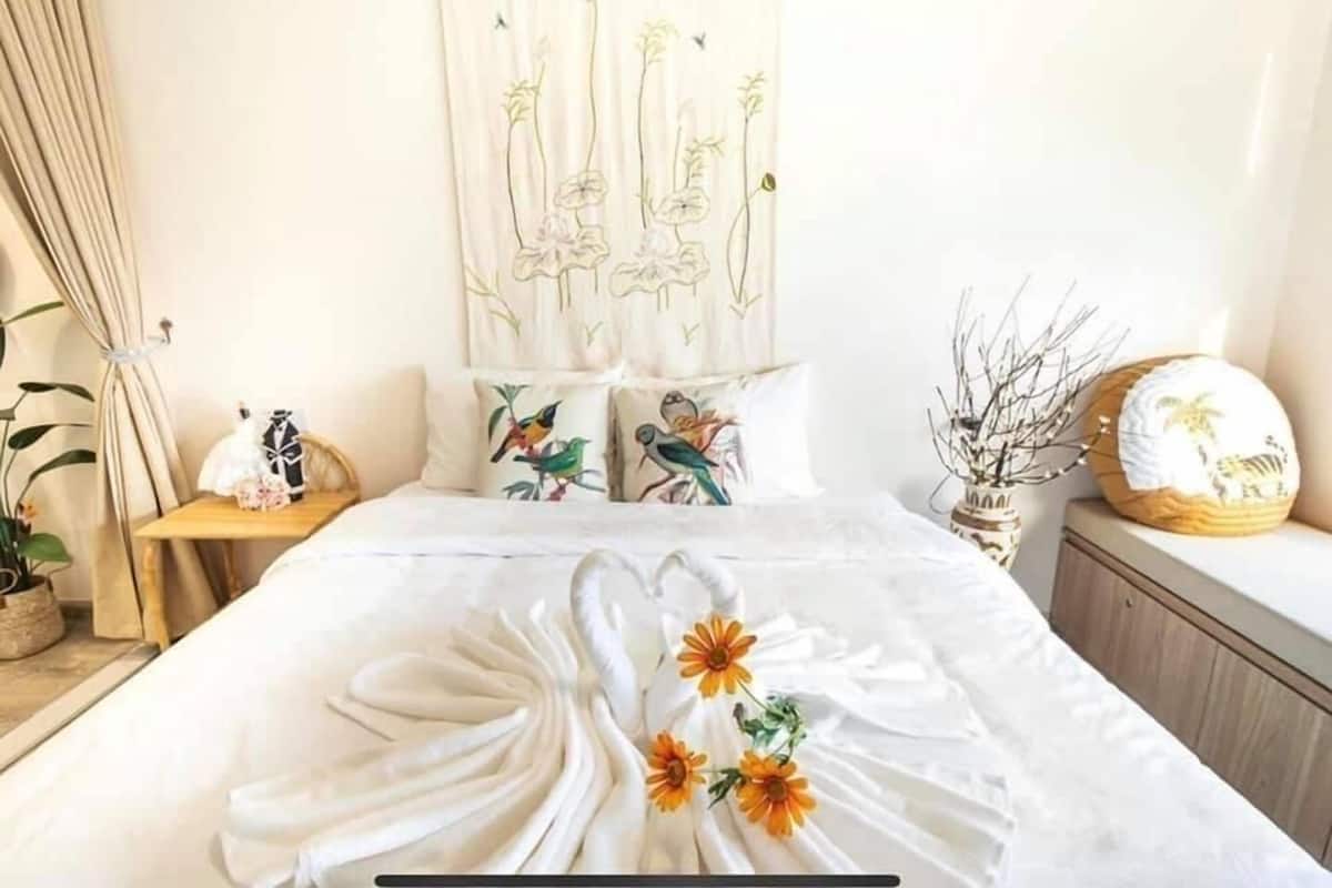 A neatly made bed with a floral bedspread, a wall tapestry with birds, and a bedside table with a vase and a decorative item.