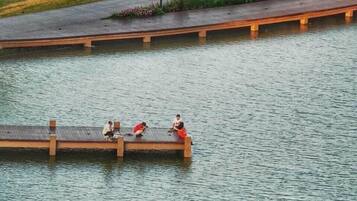 A wooden bridge over a calm body of water with three people sitting on it.