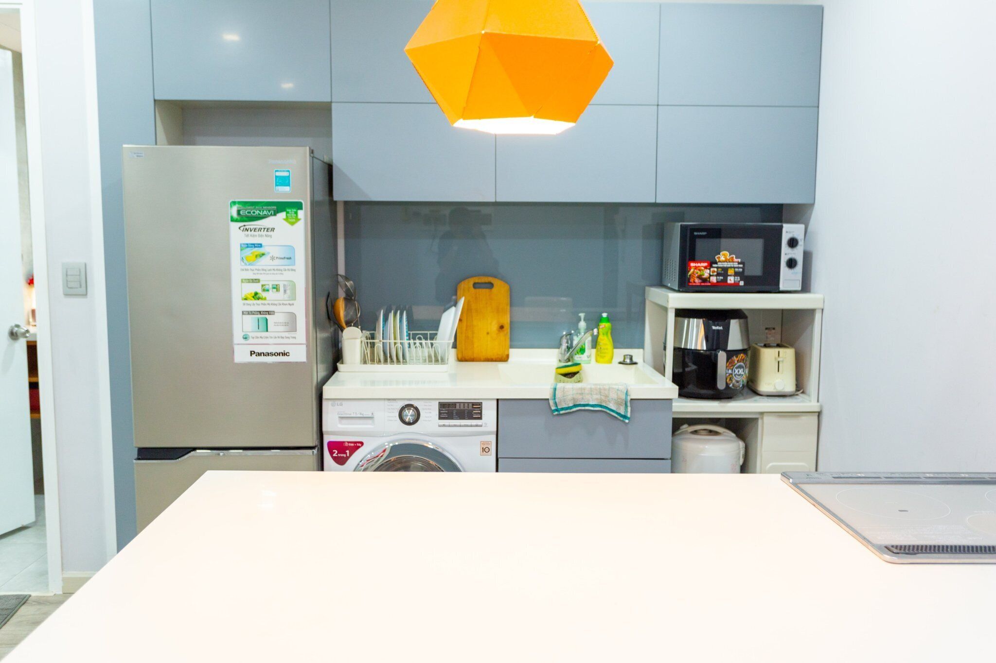 A compact kitchen with a refrigerator, microwave, washing machine, and a sink.