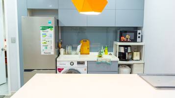 A compact kitchen with a refrigerator, microwave, washing machine, and a sink.