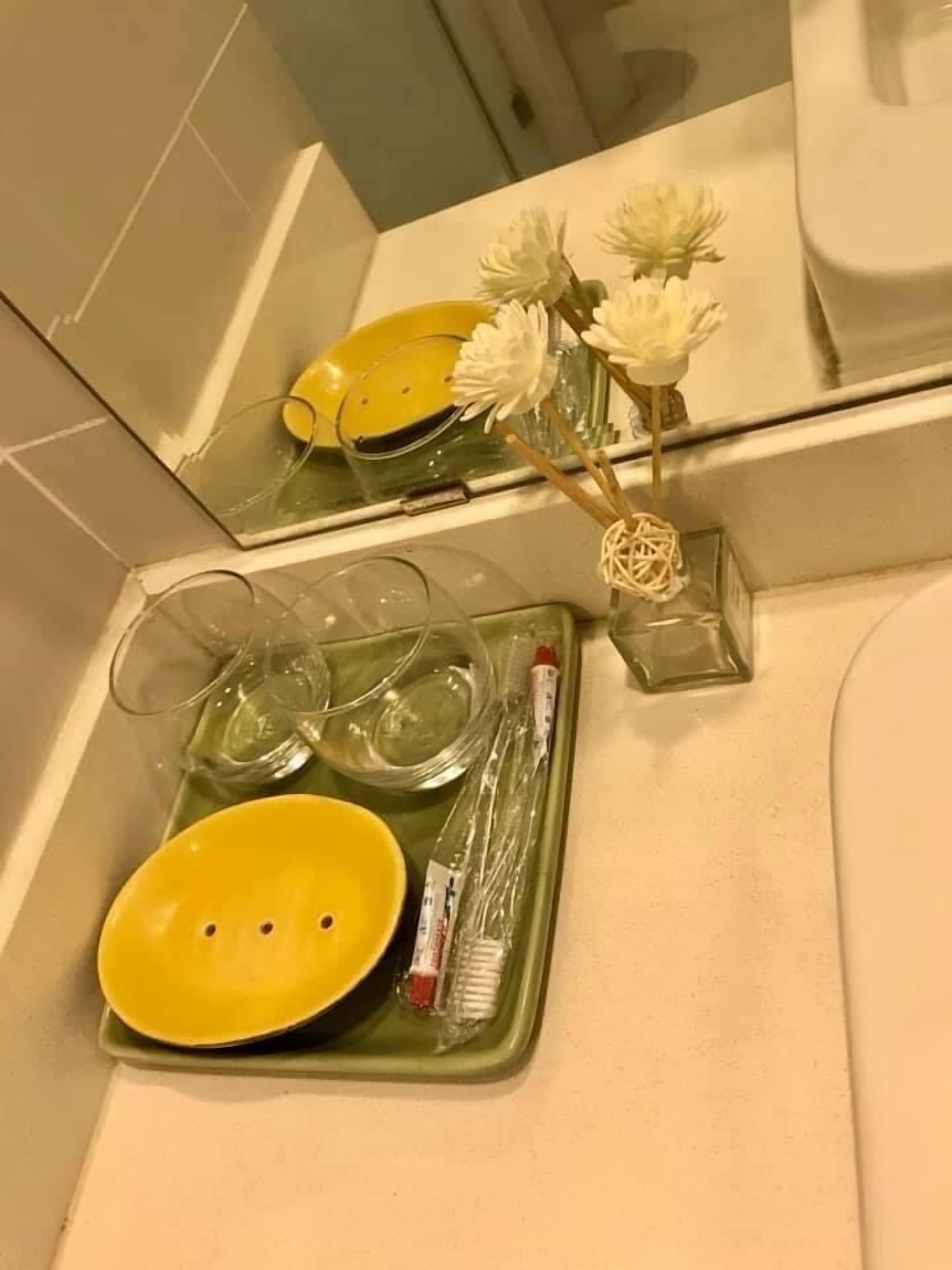 A bathroom with a mirror, a yellow bowl, a toothbrush, and a glass container.
