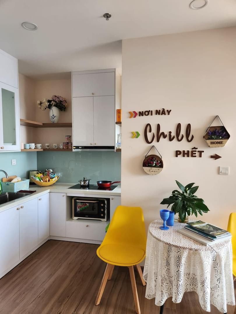A compact kitchen with white cabinets, a microwave, and a small dining area with a yellow chair and a table.