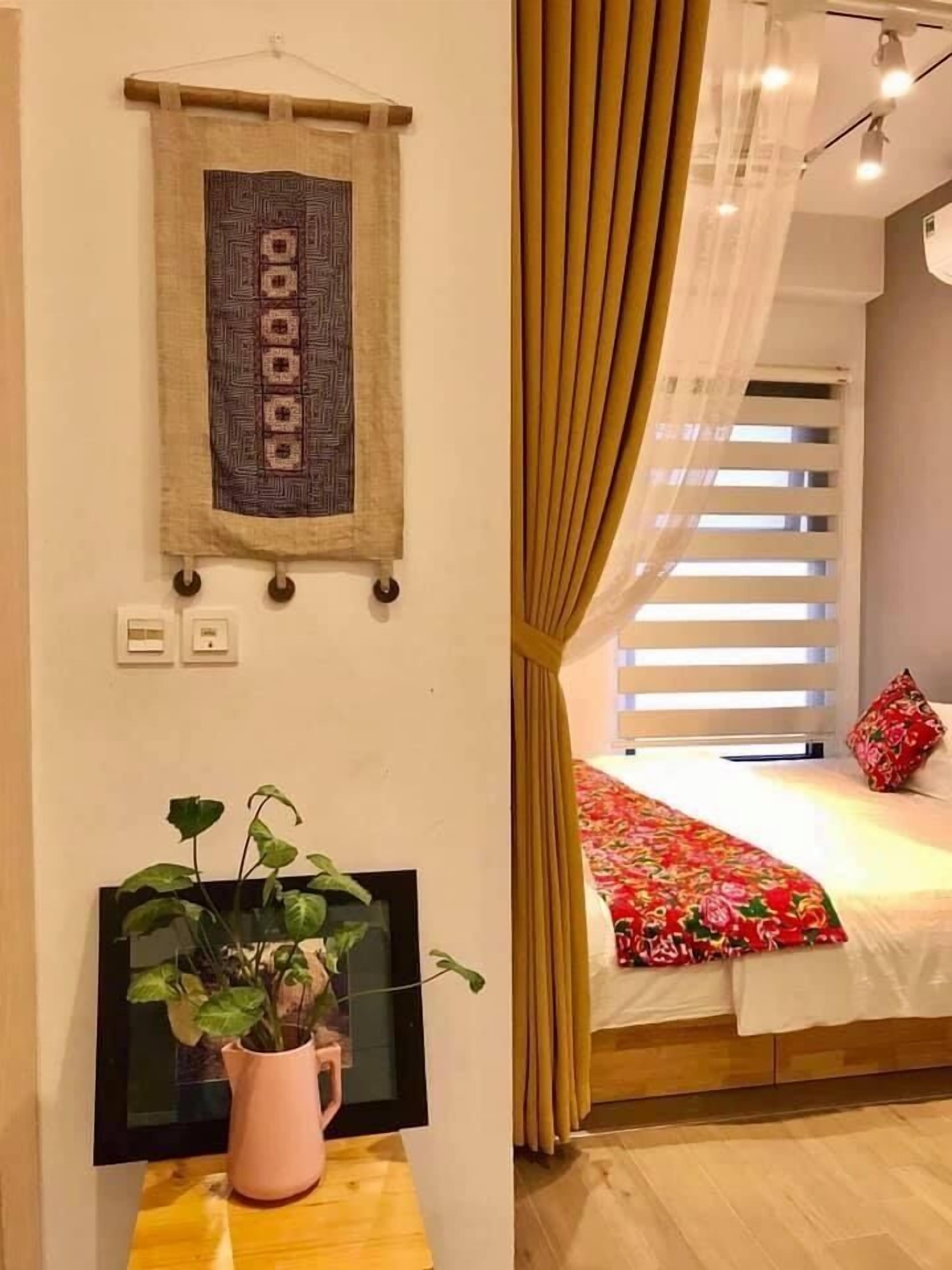 A bedroom with a bed, a wall-mounted TV, a potted plant, and a window with blinds.