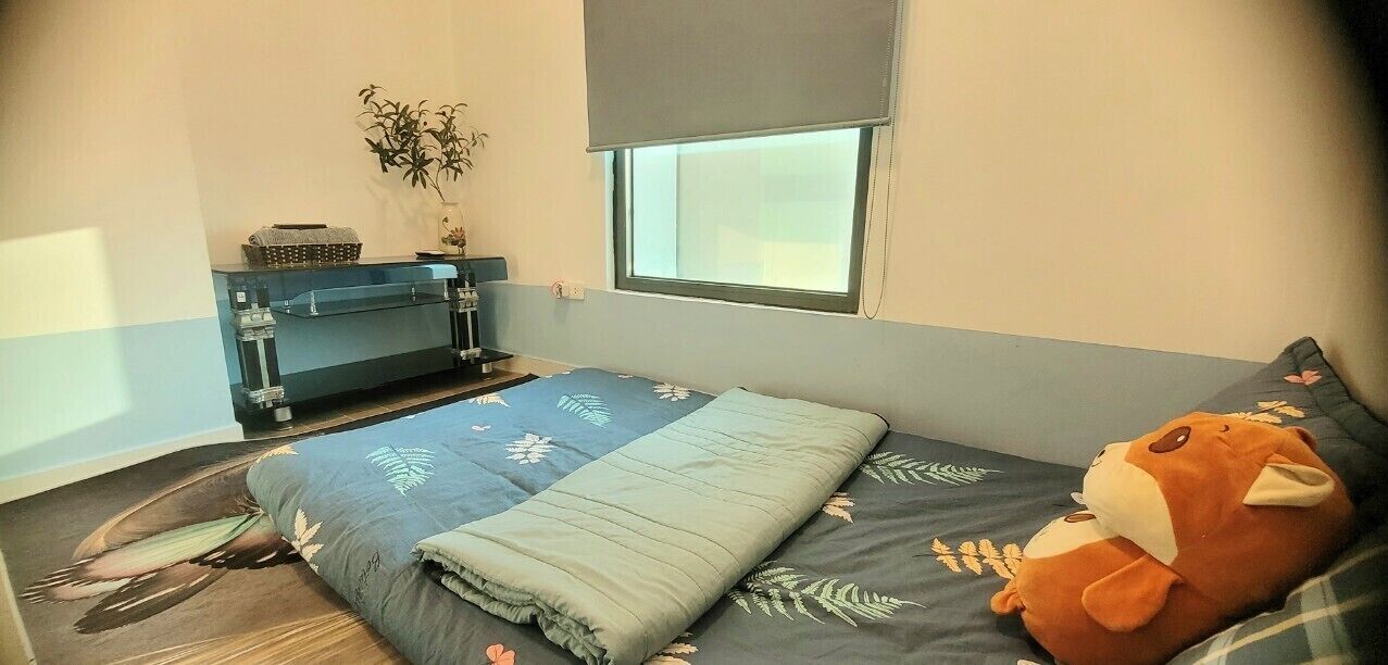 A bedroom with a bed, a window, a small table, and a plant.