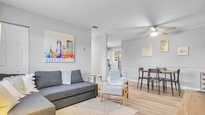 Una sala de estar moderna con un sofá gris, una mesita y un comedor con sillas.