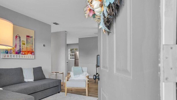 Una sala de estar moderna con un sofá gris, un sillón blanco y una obra de arte con un paisaje urbano colorido en la pared.