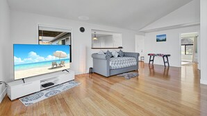 En moderne stue med et fladskærms-tv, en grå sofa, trægulv og havudsigt gennem vinduet.