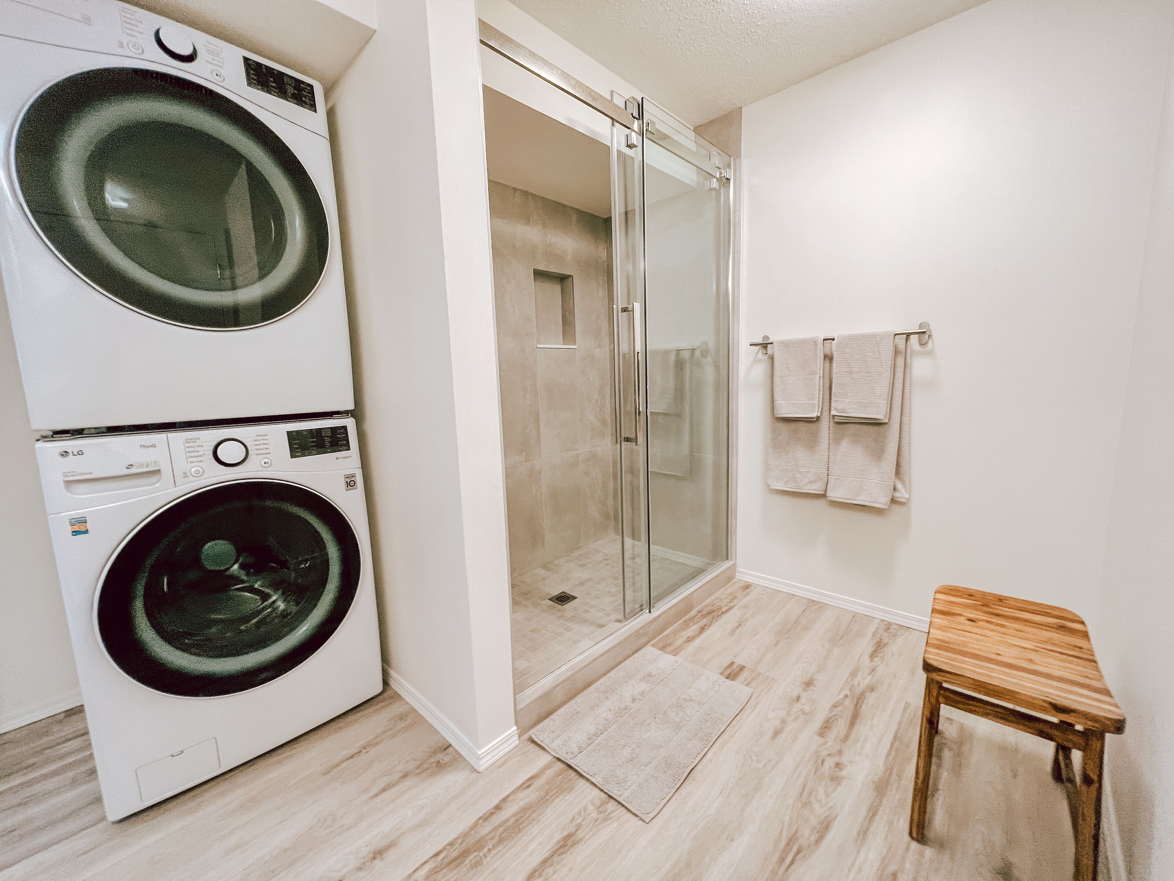 A laundry area with two washers and a dryer, a glass shower enclosure, and a small wooden stool.