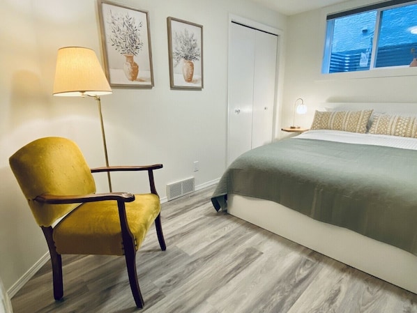 A bedroom with a bed, a yellow armchair, a floor lamp, and two framed pictures on the wall.
