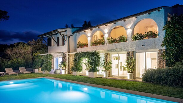 Une maison à deux étages avec une piscine, un espace salon extérieur et un jardin bien éclairé.
