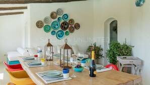 Un coin repas avec une table en bois dressée pour quatre personnes, entourée de chaises colorées. Un mur orné d’assiettes décoratives est visible derrière la table.