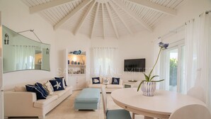 Un salon spacieux avec un haut plafond, un grand miroir, un ensemble de canapés, une table à manger avec des chaises et un téléviseur.