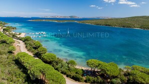 Un paysage côtier caractérisé par une eau d’un bleu limpide, un port de plaisance et une végétation luxuriante.