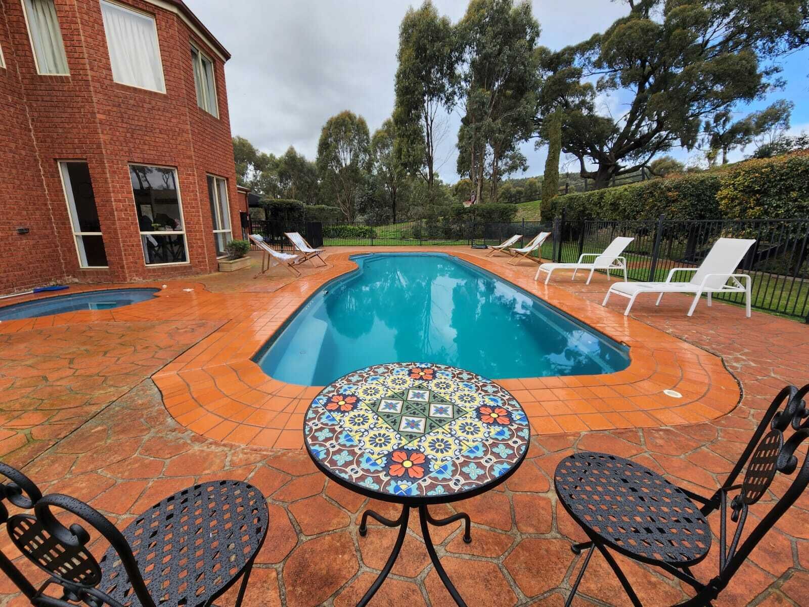 Una piscina con sillones de descanso y una mesa en un patio trasero.