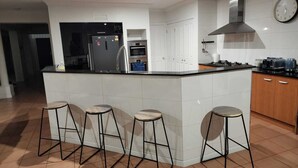 Een moderne keuken met een centraal eiland, barkrukken, een koelkast, oven, magnetron, en een klok aan de muur.