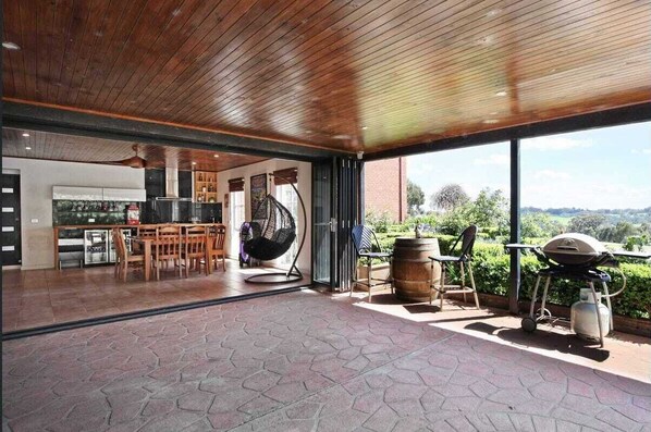 Enjoy a spacious living area with a high ceiling, kitchen, dining, and seating areas, offering a barbecue grill and a view of the outdoors.