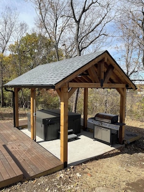 A covered outdoor grill area with a wooden deck, built-in seating, and a barbecue station.