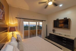 Une chambre avec un lit, une télévision, un balcon avec des rideaux et un ventilateur de plafond.
