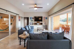 Un salon moderne avec un canapĂ©, une table basse et un tĂ©lĂ©viseur. Il y a un balcon amĂ©nagĂ© avec du mobilier dâextĂ©rieur.