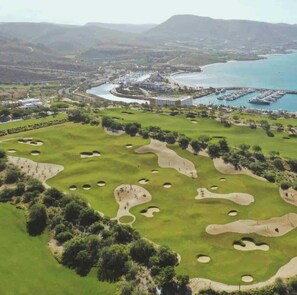 A golf course with bunkers, a marina, and a large building in the background.