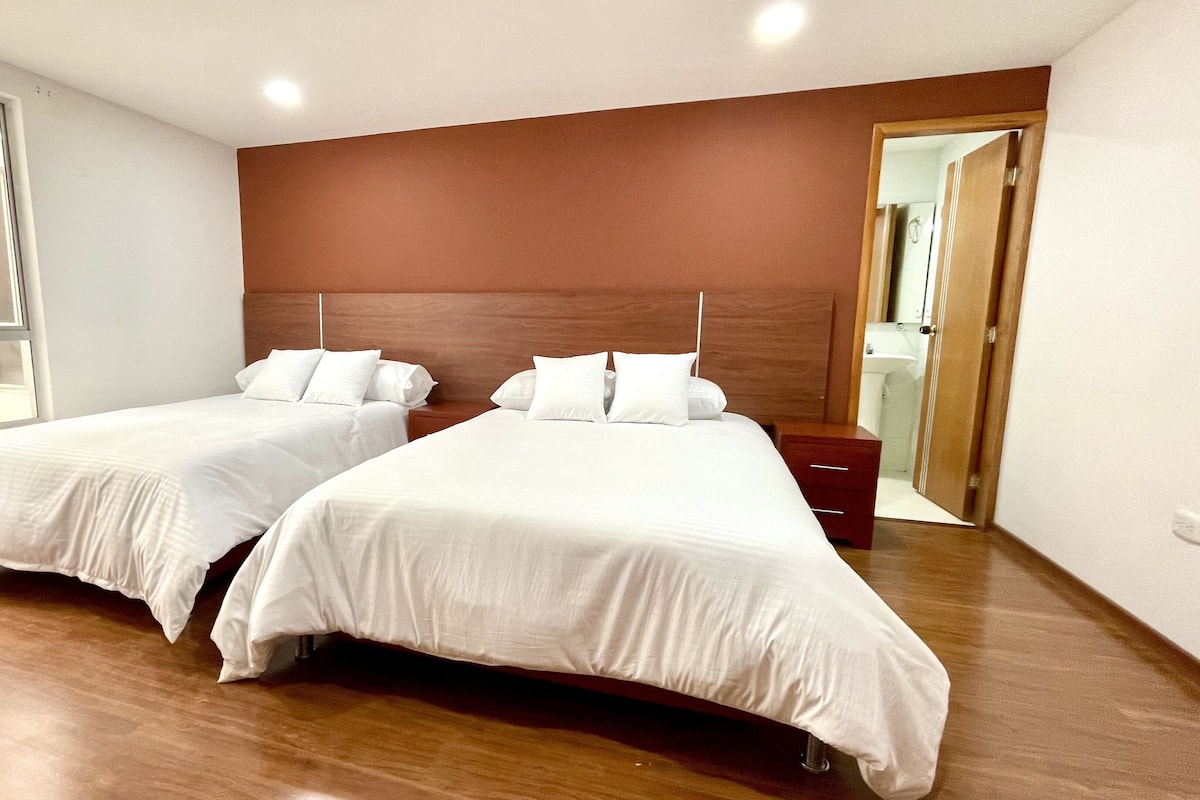 Een hotelkamer met twee bedden, houten hoofdborden, een houten vloer, een raam en een deur naar een badkamer.