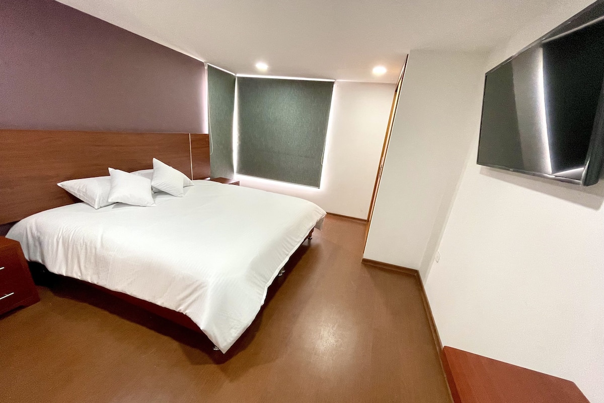 Een moderne hotelkamer met een groot bed, een houten hoofdbord, een nachtkastje en een groot raam met uitzicht.