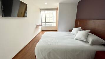 Un dormitorio con una cama grande, televisor montado, una ventana y suelo de madera.