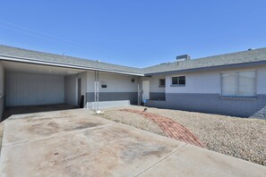 A two-story building with a garage, a covered driveway, and a gravel area.