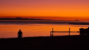 La silhouette d’une personne se tenant près d’une étendue d’eau calme, au coucher du soleil.
