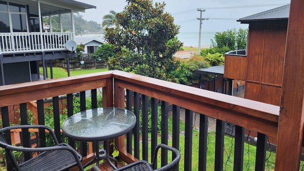 Une terrasse en bois avec une table en verre et deux chaises en osier, donnant sur un quartier résidentiel avec des maisons et un arbre.