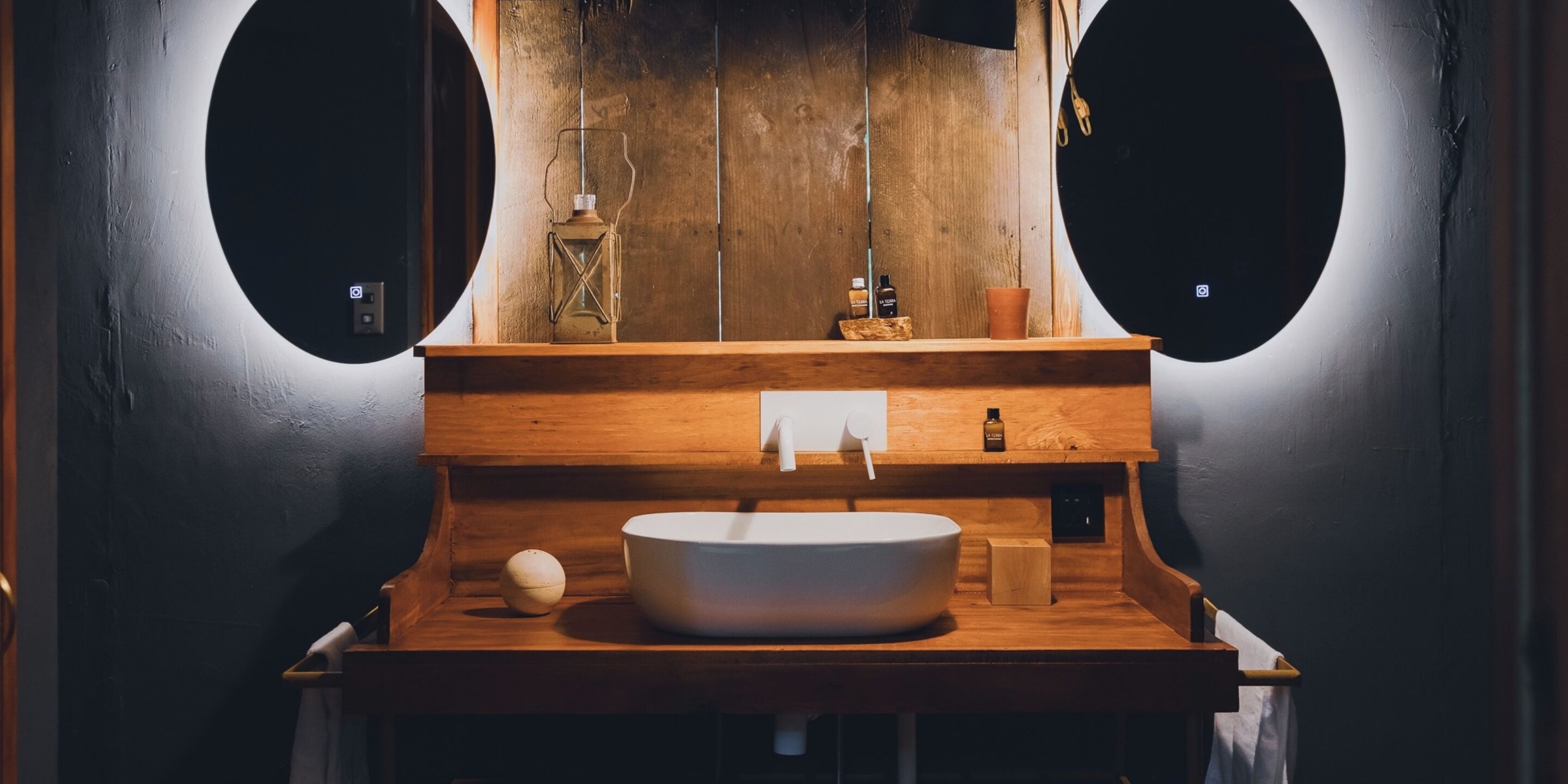 A bathroom with a wooden vanity, a round mirror, and a vessel sink.