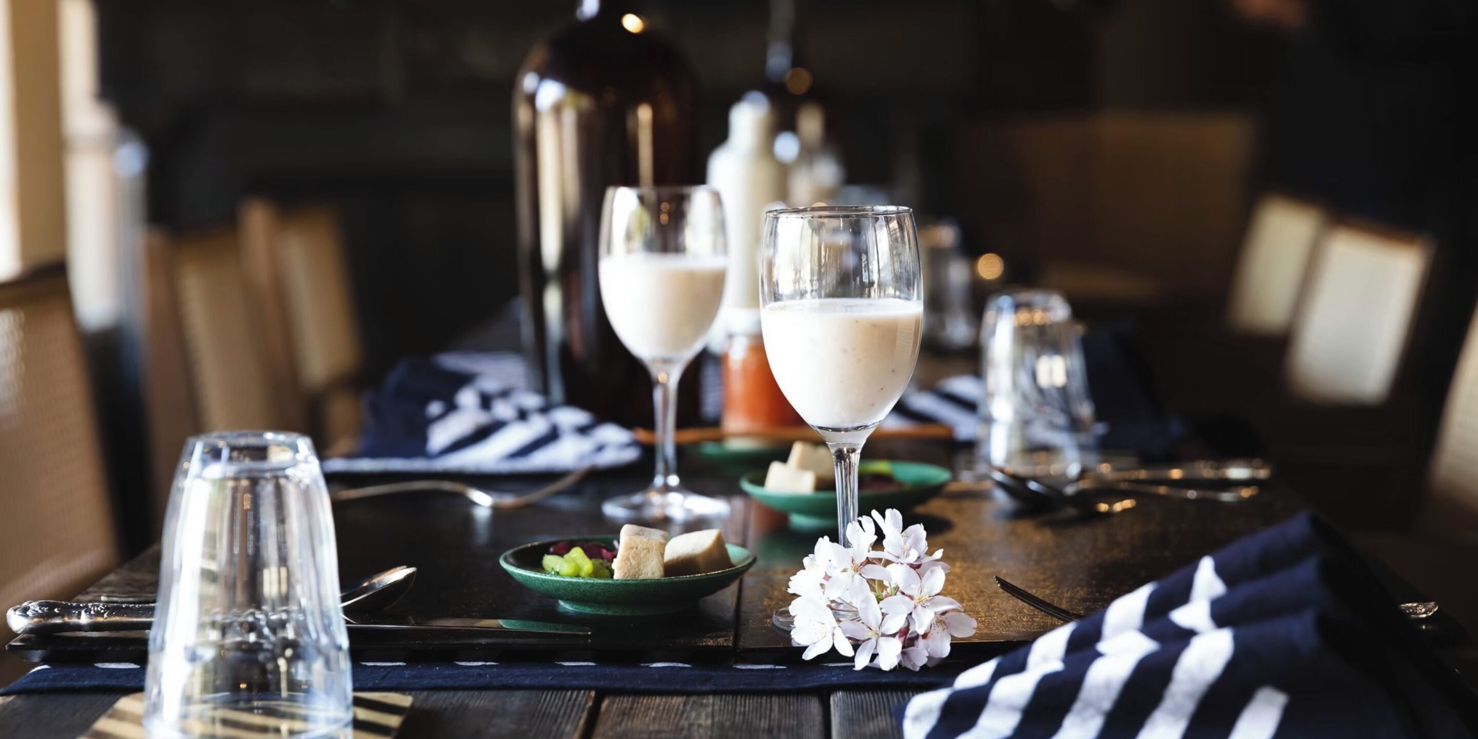 Une table à manger avec des verres contenant une boisson claire, des assiettes remplies de nourriture et une bouteille en arrière-plan.