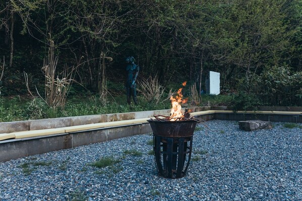 A fire pit in a gravel area with a statue and a white sign in the background. - La Terra Nagano (Shiojiri)