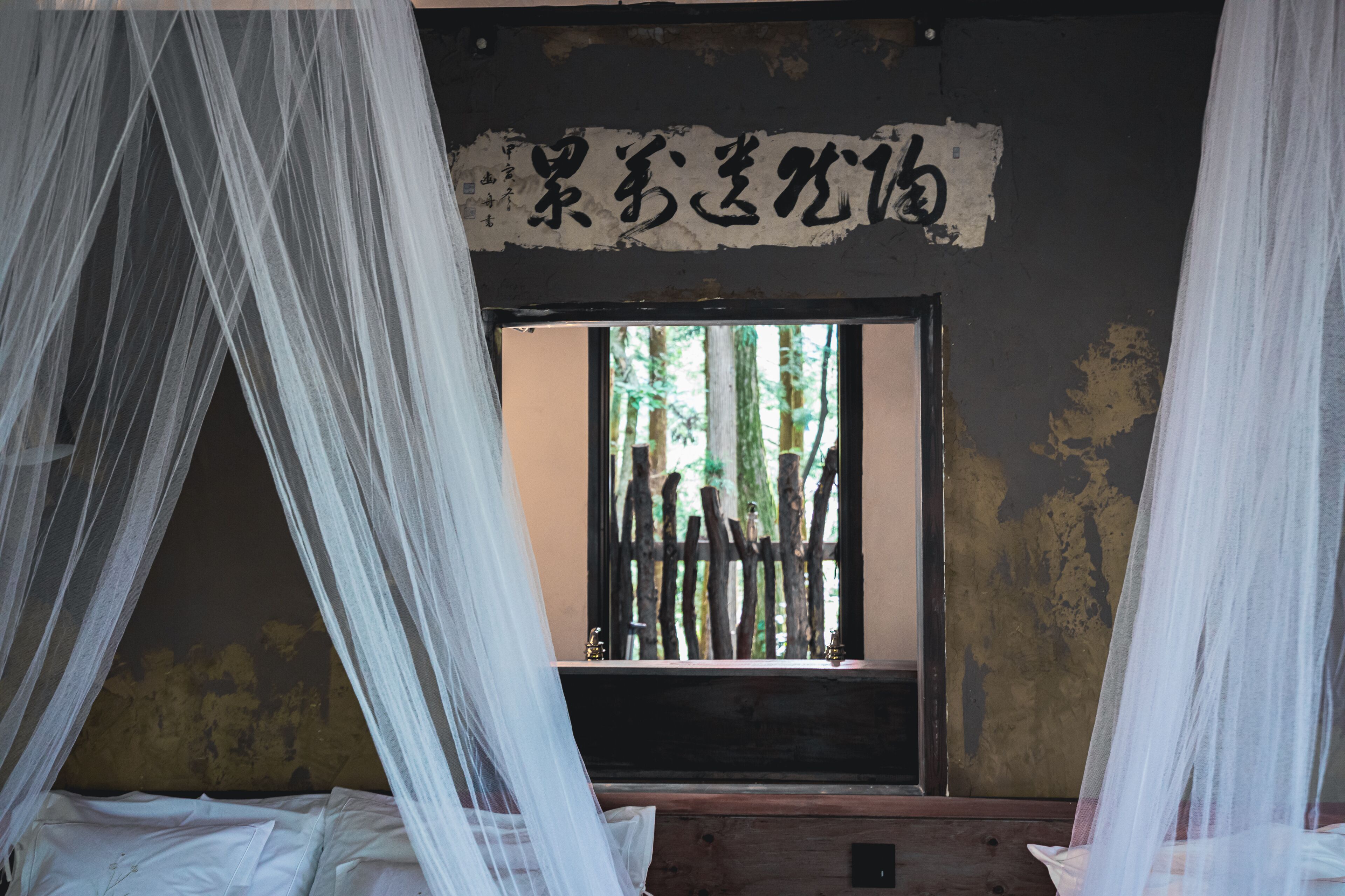 Una habitación con una cama bajo un dosel, una ventana con vistas a árboles y una pared con un letrero.