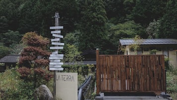 A signpost with multiple directional signs pointing to various amenities such as a glamping site, reception, lounge, wine bar, library, forest cinema, nature pool, rose farm, factory, restaurant, pizza, and BBQ.