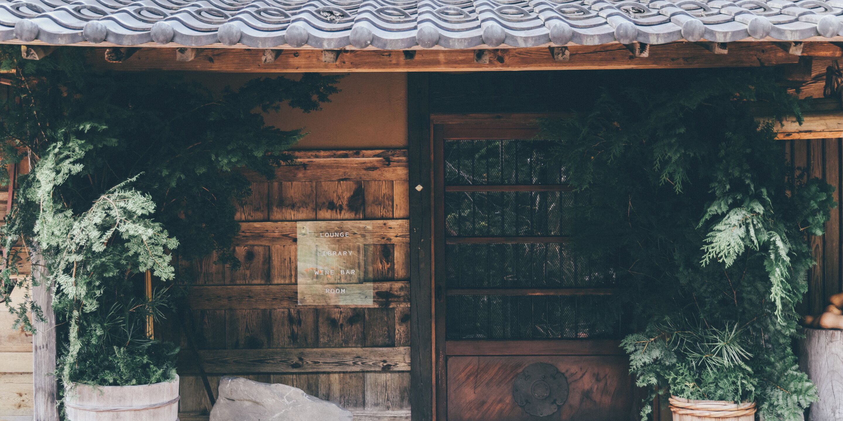 A wooden door with a frosted glass panel, flanked by potted plants.