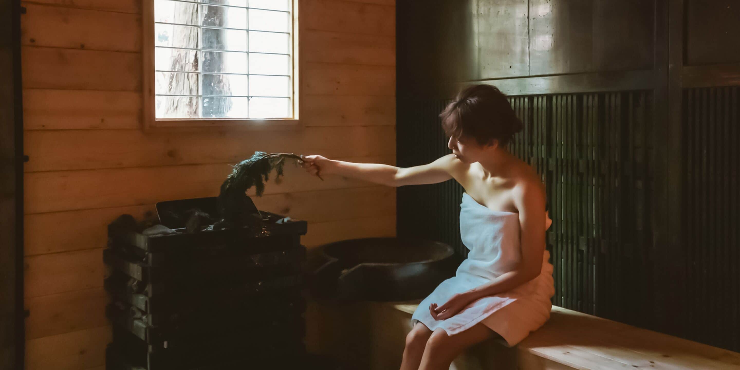 A person sitting by a window in a wooden room, reaching out to touch a water feature.