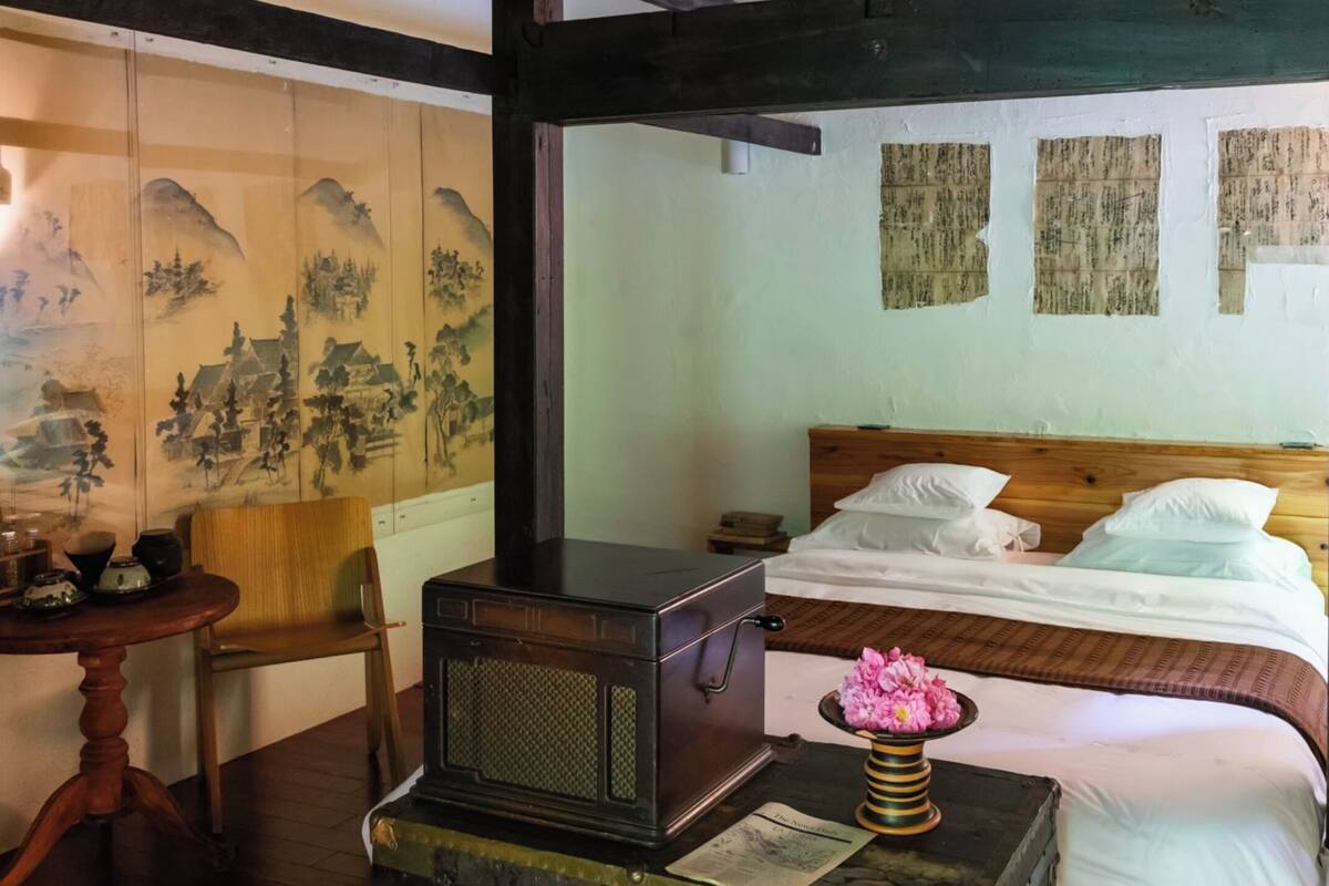 Quarto tradicional com cama, móveis de madeira e objetos decorativos.