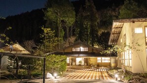 A traditional Japanese-style building with a wooden exterior and a tiled roof, surrounded by trees and a stone pathway leading to the entrance. - La Terra Nagano (Shiojiri)