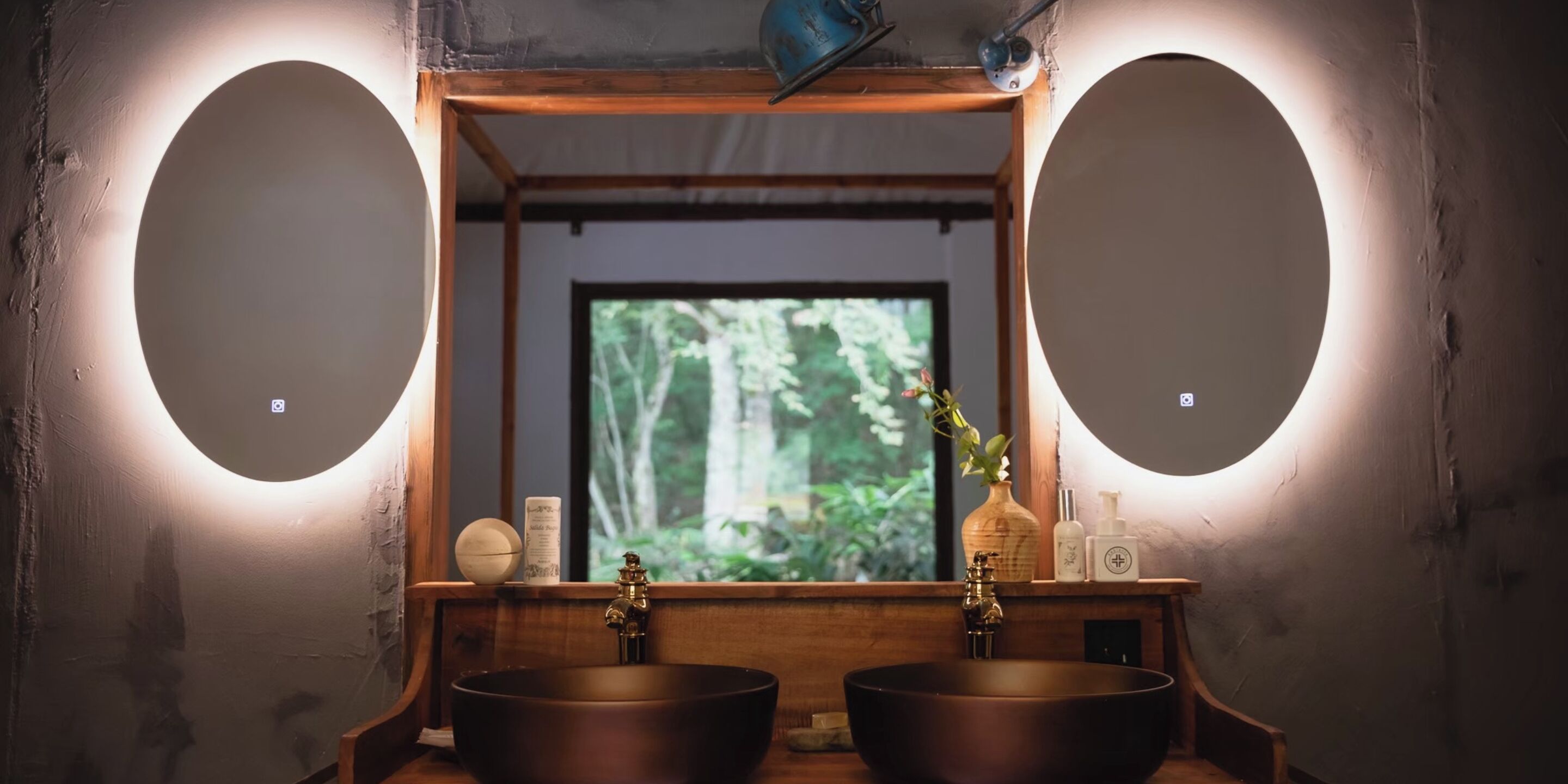 A bathroom with two sinks, a mirror, and a window with a view of trees.