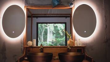 A bathroom with two sinks, a mirror, and a window with a view of trees.