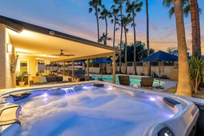 Un bain à remous doté d’un espace détente couvert, une piscine et des palmiers en arrière-plan.