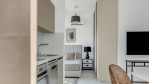 A modern hotel room with a kitchenette, a bed with a headboard, a bedside table with a lamp, and a flat-screen TV. - Sanders Elgio - Adorable Studio with Balcony (Agios Athanasios)