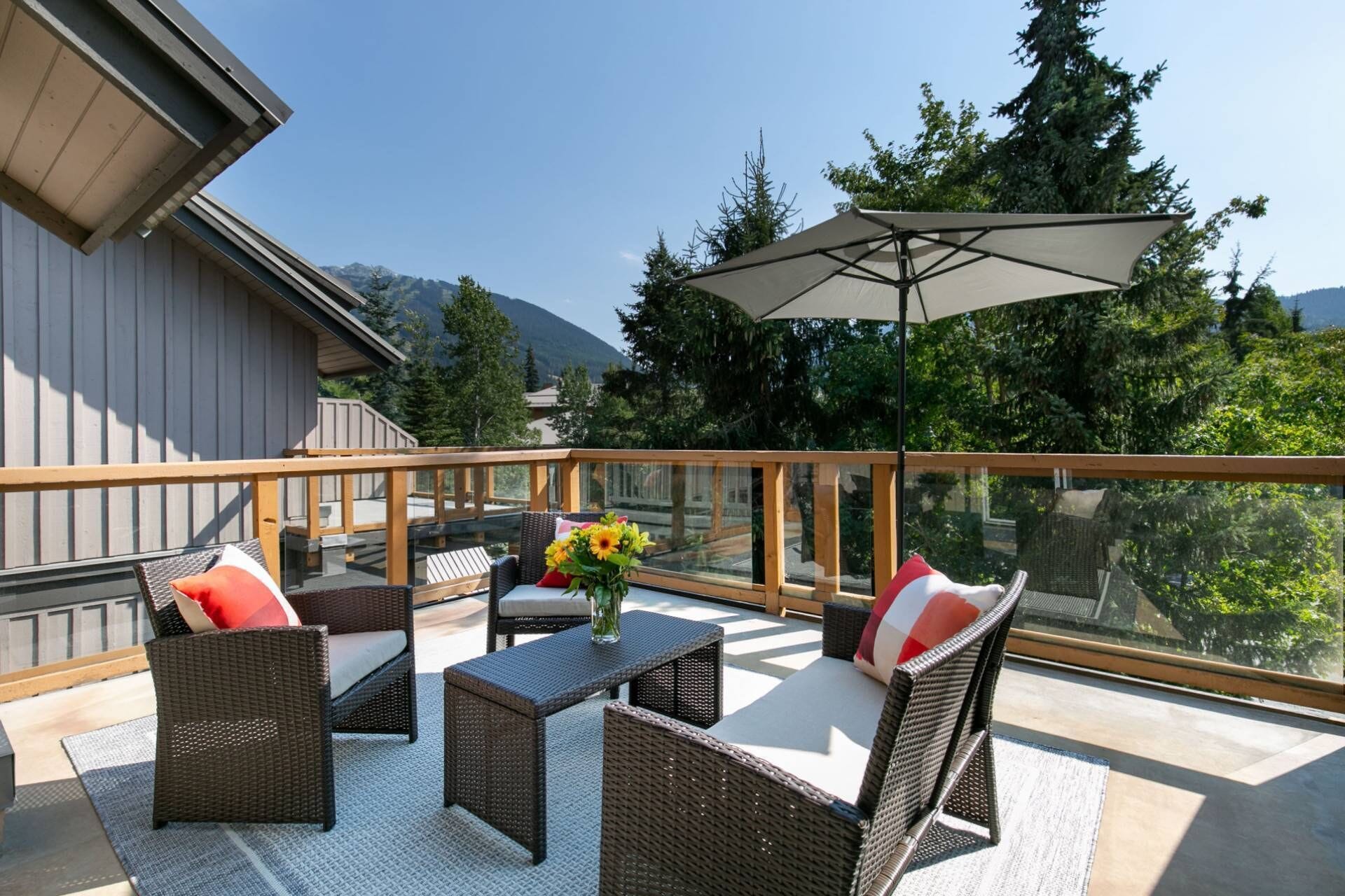 A balcony with wicker furniture, a table with a vase of flowers, and a large umbrella.