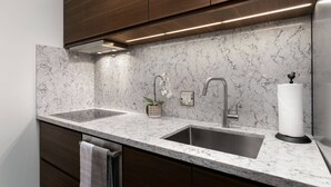 Una cocina con dos fregaderos, gabinetes de madera oscura, un salpicadero de mármol e iluminación debajo de los armarios.
