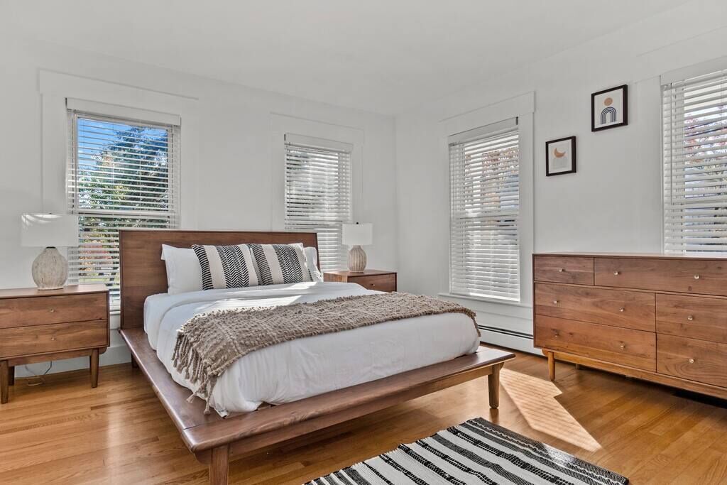 Quarto com cama de madeira, paredes brancas e cômoda de madeira.
