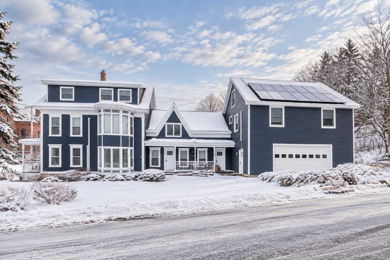 A two-story house with a garage, a bay window, and a solar panel on the roof.