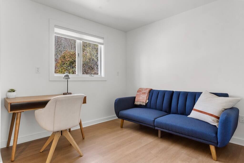 A room with a desk, a blue sofa, and a window with a view of trees.
