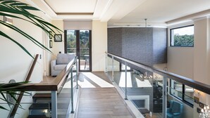 A modern interior with a staircase leading to a balcony, a seating area, and a view of the outdoors. - Heated pool, kids pool, gorge and sea views! (Rethymno)